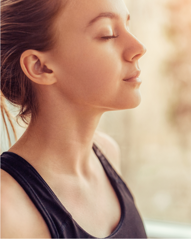 Woman with eyes closed, wearing a black tank top, against a blurred natural background